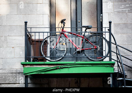 Red city bicycle parked in front of an old apartment door next to the staircase in Montreal, Canada Stock Photo