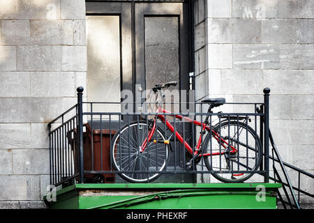 Red city bicycle parked in front of an old apartment door next to the staircase in Montreal, Canada