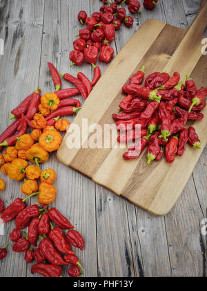 Top down view on arrangement of different colorful chilies on a table with wooden board Stock Photo