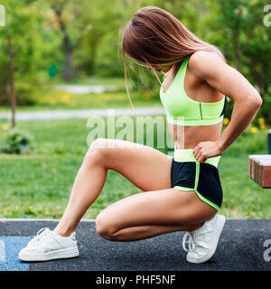 Young sporty woman doing triceps dip exercise on city street bench. Stock Photo