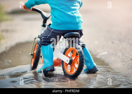 child on a bicycle. Boy in wellies in puddle on rainy weather Stock Photo
