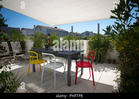 The terrace of a flat furnished with a set of garden furniture, deck chairs and a sun shade sail. Stock Photo