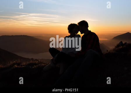 the silhouette of a couple enjoying a moment of intamacy with the backdrop of a beautiful sunset in the mountains of Italy Stock Photo