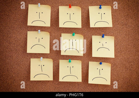 Notes with sad faces on bulletin board. Close up. Stock Photo