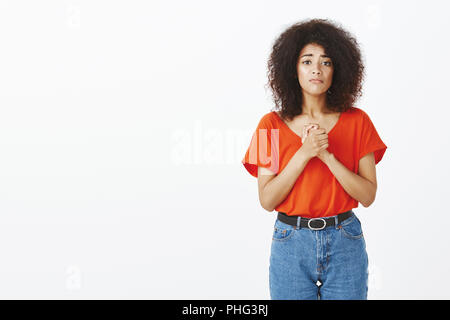 Beg you to help me. Portrait of good-looking curly-haired woman, holding hands clenched on chest, asking for forgiveness or apology, standing over gray background worried and moving Stock Photo