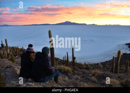 A couple enjoy sunrise views of the Salar de Uyuni from Isla Incahuasi. Uyuni, Bolivia Stock Photo