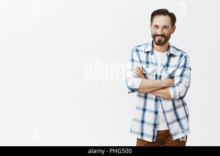 Sons always can lean on dad. Portrait of handsome and confident friendly-looking old male with beard and moustache, holding hands crossed on chest and smiling, standing in elevetor over grey wall Stock Photo