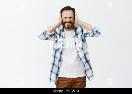 Man suffering from loud voices in head, being displeased and miserable. Distressed intense adult man with disease, holding palms on ears, closing eyes tight and clenching teeth from painful feeling Stock Photo