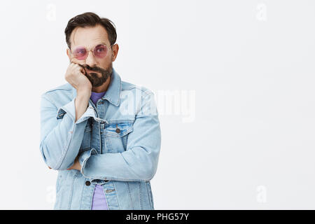 Man thinking how old is he, being sad and gloomy growing up and becoming grandad. Portrait of upset good-looking mature man with beard and moustache spacing out, staring aside in sunglasses Stock Photo