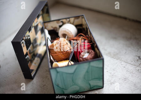 Assorted twines, string and thread rolls in an open container viewed from high angle view on a corner shelf below a vintage window under daylight with Stock Photo