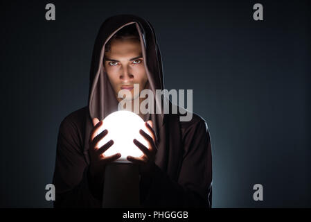 Young wizard with crystal ball in dark room Stock Photo
