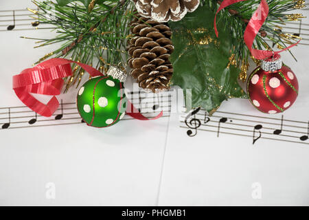 red and green Christmas ornaments and ribbon with pine on sheet music Stock Photo