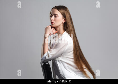 side profile view of calm beautiful young model actor with long brown hair in white t-shirt sitting with closed eyes and touching her chin with seriou Stock Photo