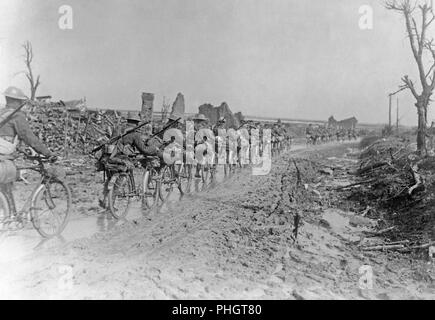 First World War 1914-1918. British soldiers with their bicycles are walking on a muddy road somewhere in France. They are passing demolished buildings and ruins. Stock Photo