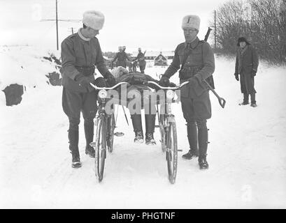 1940s soldiers. The swedish army is being mobilized during the World War II. Soldiers are on a winter exercise and trying out a bicycle carried stretcher with a soldier lying on it.  Sweden 1941.  Photo Kristoffersson 211-7 Stock Photo