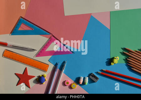 Colour pencils, graphite pencils, erasers, sharpener, set squares, ruler and a biro on a multicoloured background of colourful paper. Flat lay Stock Photo