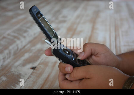An old fashioned Nokia flip phone in a woman's hands, against a wooden tabletop background with copy space Stock Photo