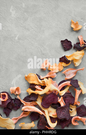 Various vegetable chips on grey background, copy space. Assorted dehydrated beetroot, carrot, pumpkin vegetable chips - healthy vegan snack. Stock Photo