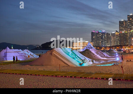 Haeundae Sand Festival 2018, Busan, Korea. Sculptures lit at twighlight with bay, Dongbaek Park and skyscrapers in background; lighthouse Stock Photo