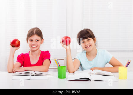 Cute little girls are having healthy snack while they are doing homework. Stock Photo
