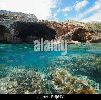 Rocky coast with large cave on the sea shore and fish underwater, split view above and below water surface, Mediterranean, Costa Blanca, Javea, Spain Stock Photo