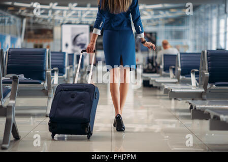 Air hostess with suitcase going between seat rows in airport. Stewardess with baggage, flight attendant with hand luggage, aviatransportations job Stock Photo