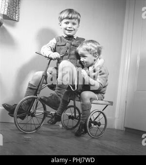 1940s children. Two boys are playing on a tricycle. The older brother is pedaling and the younger brother is sitting on the back. Sweden 1944.  Photo Kristoffersson ref M122-6 Stock Photo