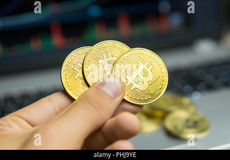 Male businessman hand holding tree bitcoin on a background of growth graph on a screen of laptop. Virtual money concept and Financial growth concept on chart background. Trading Mining of bitcoins Stock Photo