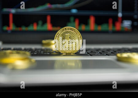 Golden Litecoin coin with gold coins lying around on a black keyboard of silver laptop and diagram chart graph on a screen as a background. Mining of litecoins online bussiness. Trading Stock Photo
