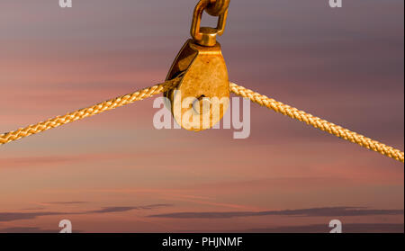 An old rusty pulley with a rope against blue background Stock Photo