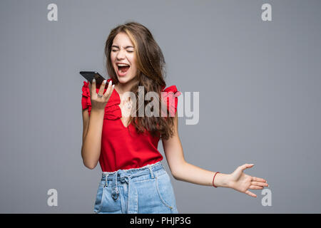 Angry woman shouting on smartphone standing over gray background Stock Photo