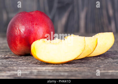 cut into pieces for convenience ripe peach, lies on a wooden table in black color Stock Photo