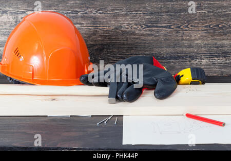 lying on a wooden table an orange construction helmet, pine boards, nails and a hammer and black gloves are used for construction work, closeup, a she Stock Photo