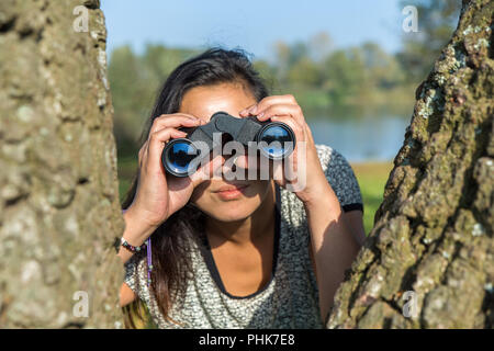 Woman looking through binoculars  near trees Stock Photo