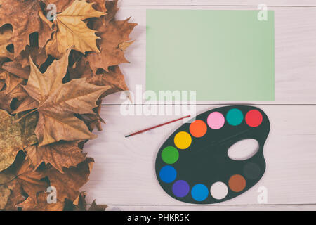 Image of watercolor paints on wooden table with autumn leaves.Image is intentionally toned. Stock Photo