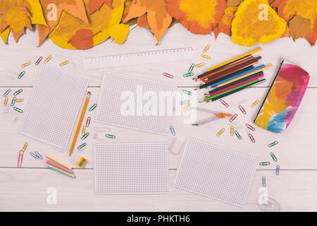Empty white papers and school supplies on wooden table with painted leaves. Stock Photo