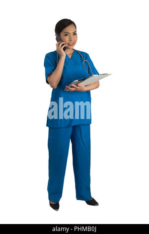 Busy female doctor in blue uniform standing while her hands holding tablet, clipboard and mobile phone on white background. Stock Photo