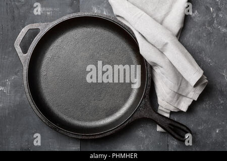 Empty, clean black cast iron pan or dutch oven top view from above on black wooden table with grey kitchen towel Stock Photo