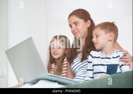 beautiful family mother and two children watching on laptop screen internet online Stock Photo