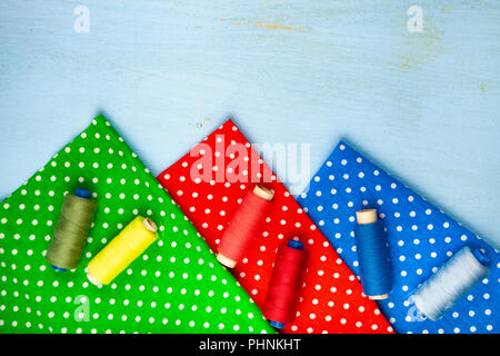 Coils with threads and multi-colored fabrics on a blue wooden background. Fabrics and thread. Stock Photo
