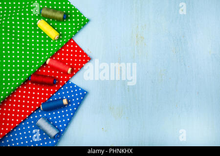 Coils with threads and multi-colored fabrics on a blue wooden background. Place for your text.Fabrics and thread. Stock Photo
