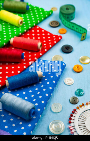 Sewing accessories and multi-colored fabrics on a blue wooden background. Fabrics, measuring tape, pins, buttons and thread. Stock Photo