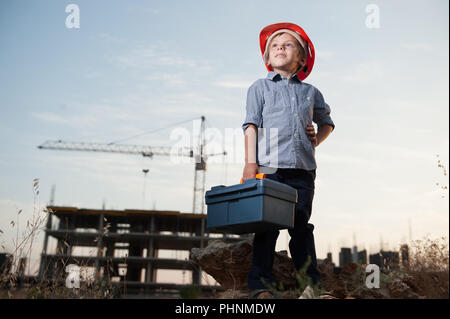 cute little kid in builder helmet with toolbox in hand on standing construction site Stock Photo