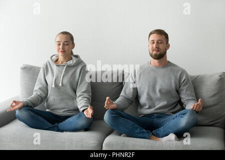 Calm couple meditating practicing yoga on couch together Stock Photo