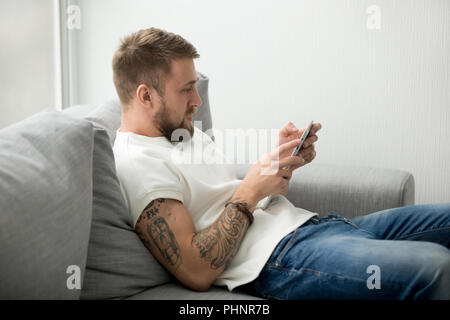 Millennial man sitting on couch holding tablet browsing web Stock Photo