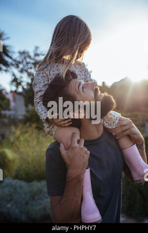 Portrait of a father carrying his daughter on shoulders at field. Little girl riding on father's shoulders. Stock Photo