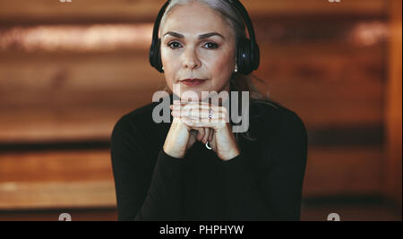 Closeup portrait of senior woman listening music on headphones. Beautiful mature woman listening to music in headphones at cafe. Stock Photo
