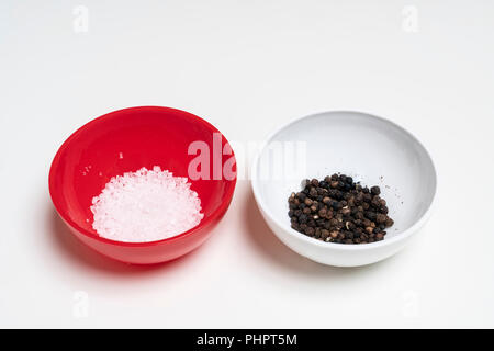 two colored bowls containing coarse salt and peppercorns Stock Photo