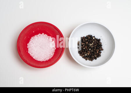two colored bowls containing coarse salt and peppercorns Stock Photo