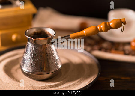 Angled view of small metal container with in front of blurred coffee mug on top of white mat and coffee grinder Stock Photo